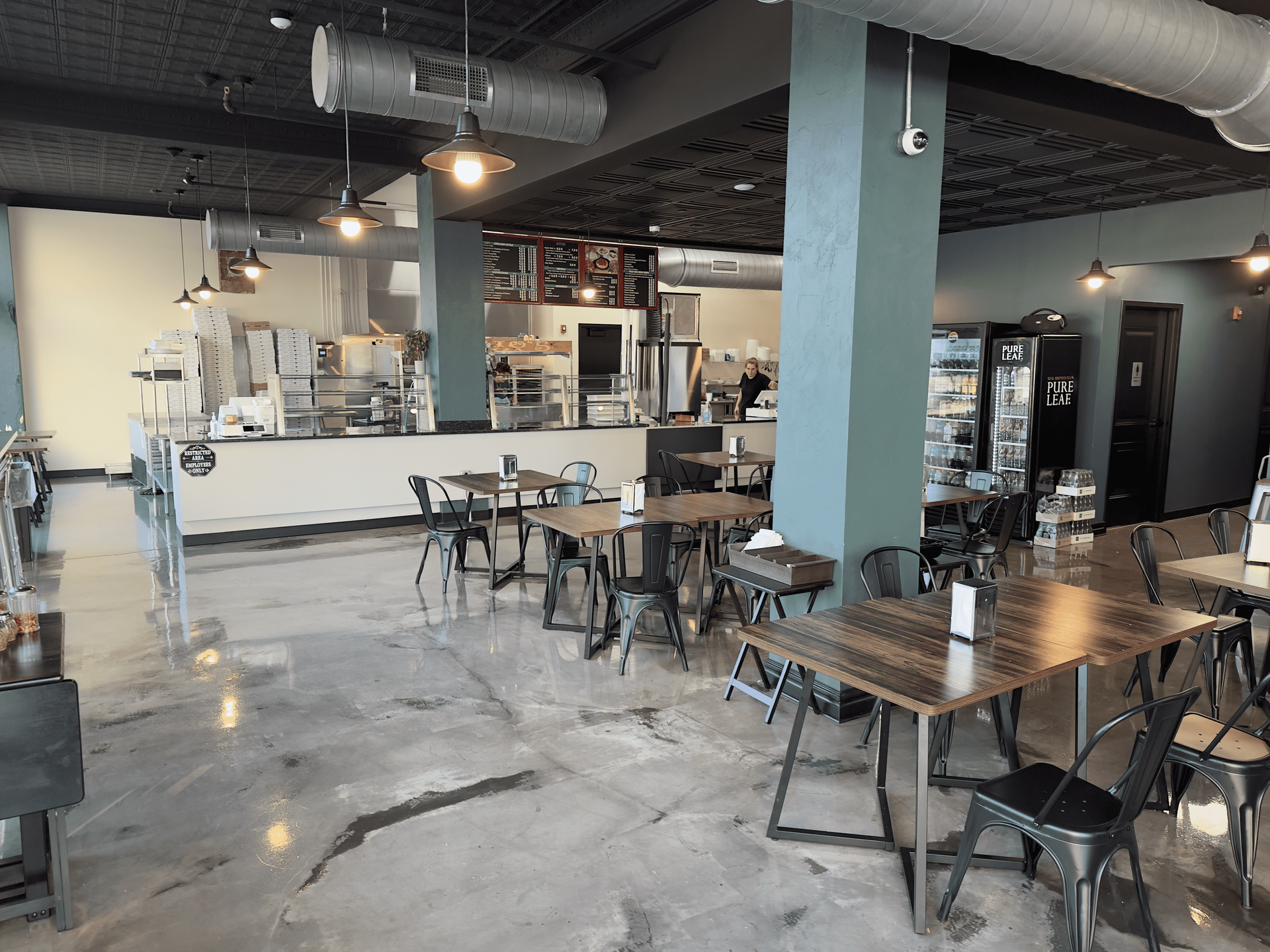 Modern café interior with wooden tables, black chairs, concrete floor, and a white service counter