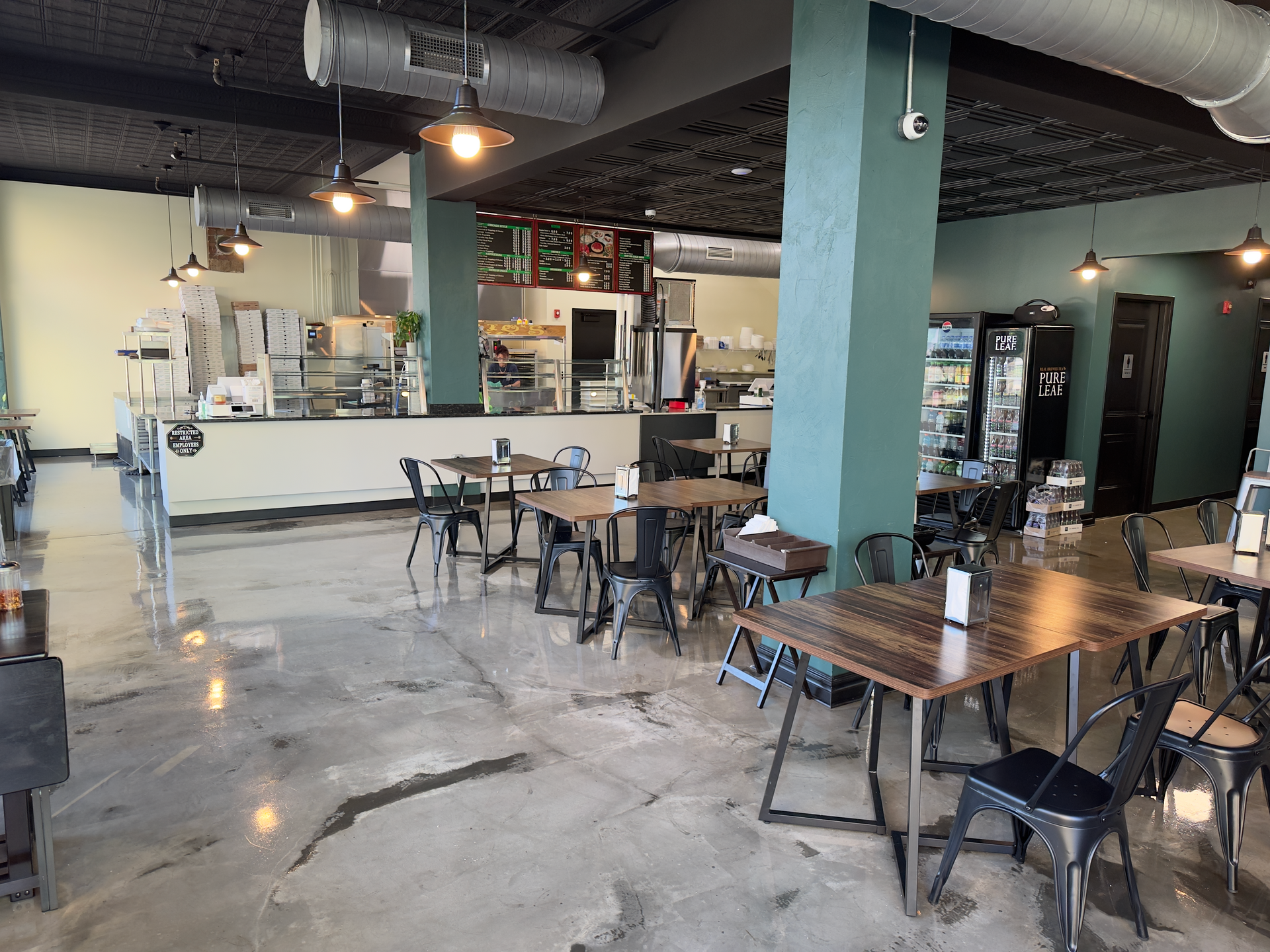 Industrial-style cafe with tables and chairs, concrete floor, and a counter in the back