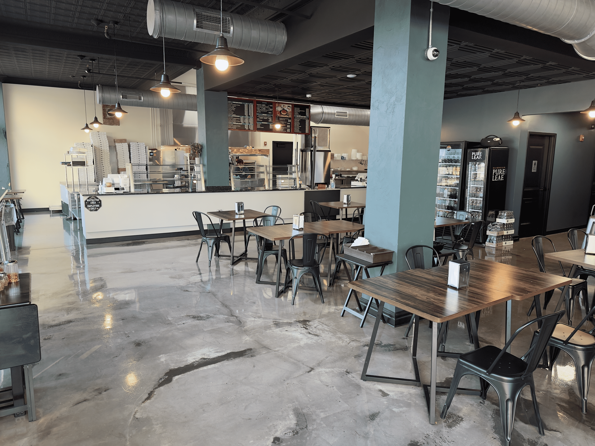 Empty café interior with metal tables and chairs, polished concrete floor, and an open counter area