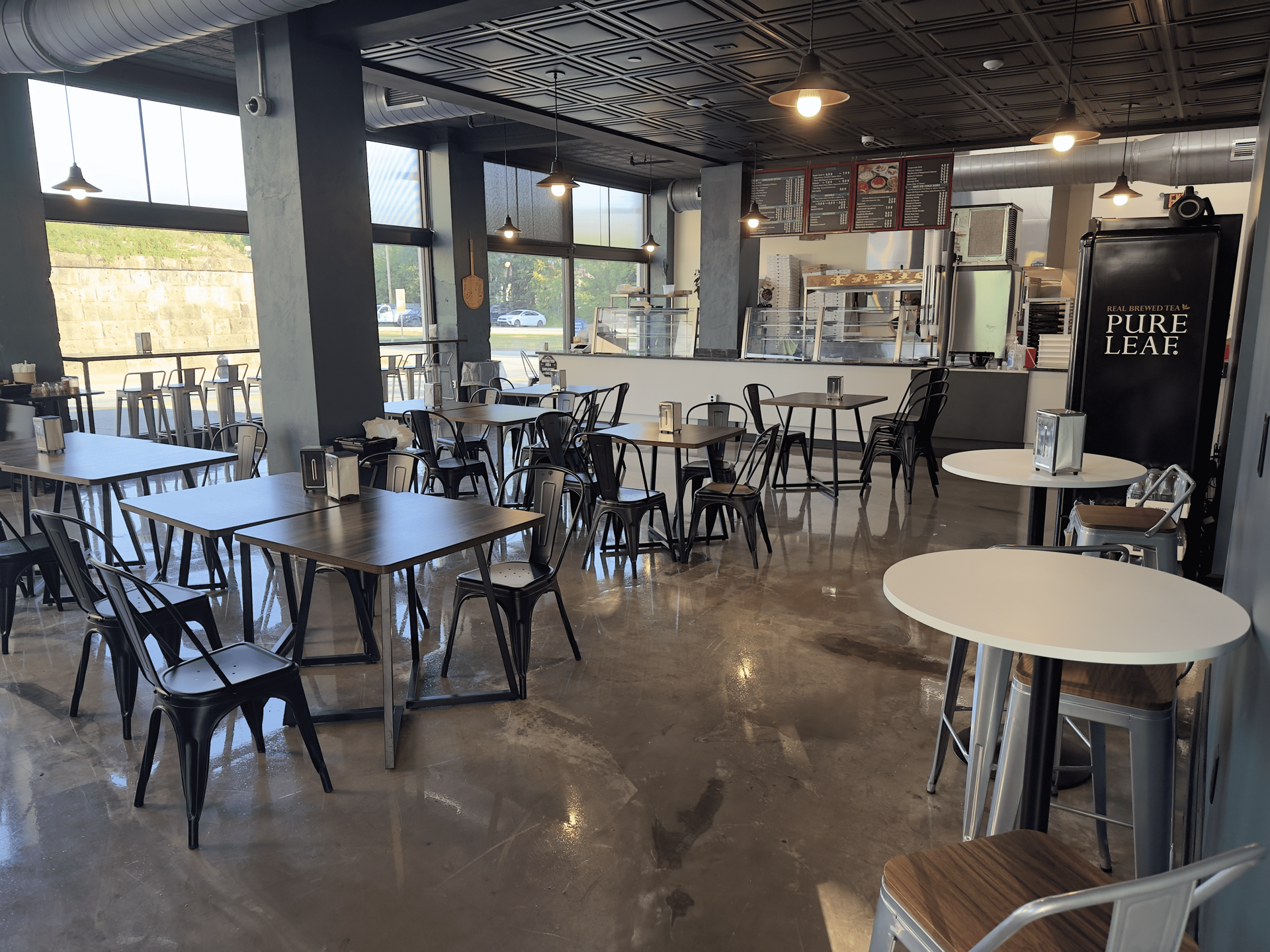 Empty modern café with black chairs, marble tables, and a patterned ceiling.