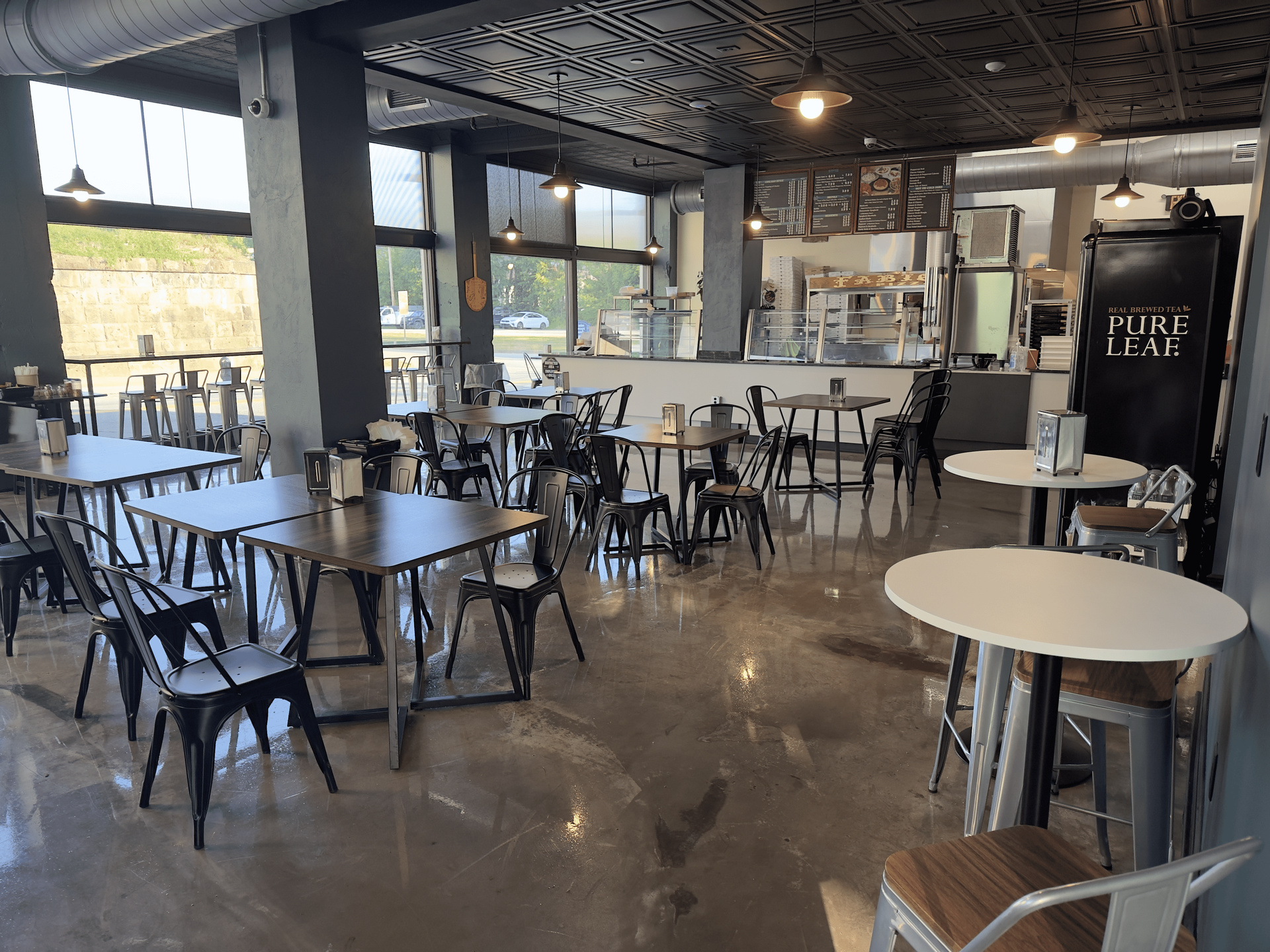 Modern café interior with scattered tables and chairs, polished floor, and patterned ceiling accents.