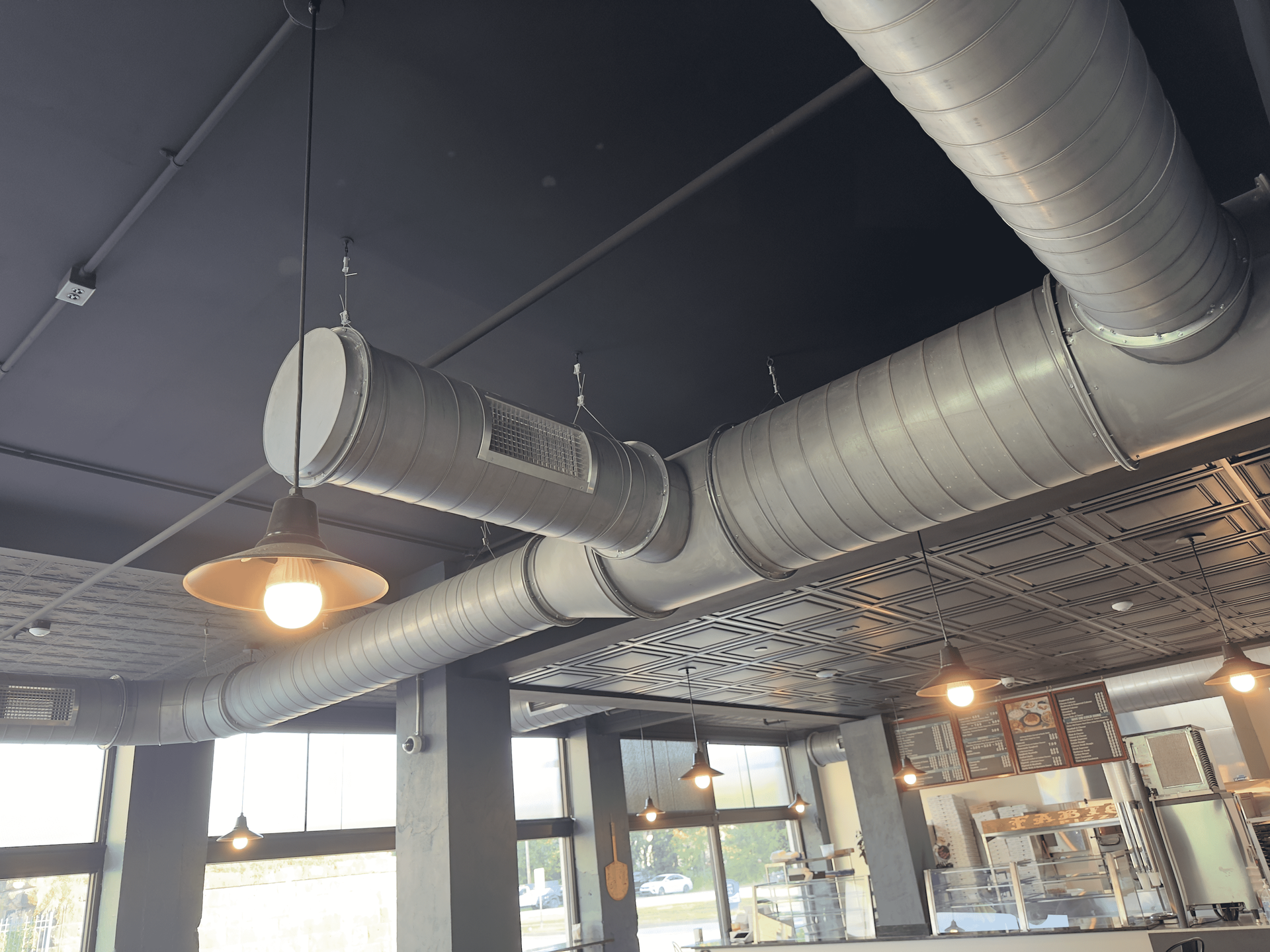 Industrial ceiling with exposed silver ductwork, dark ceiling, and warm hanging lights in a modern interior