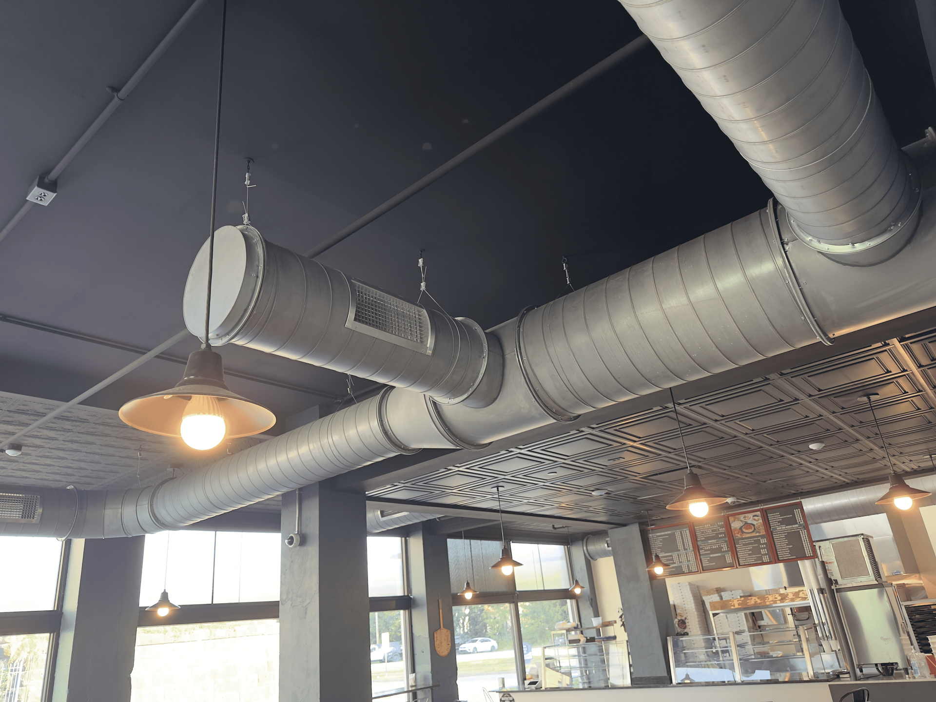 Industrial ceiling with exposed ductwork and hanging lights inside a modern interior.