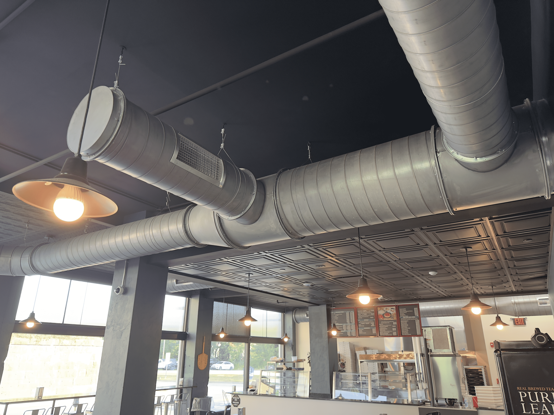 Industrial-style café interior with exposed ducts, hanging lights, and bright windows