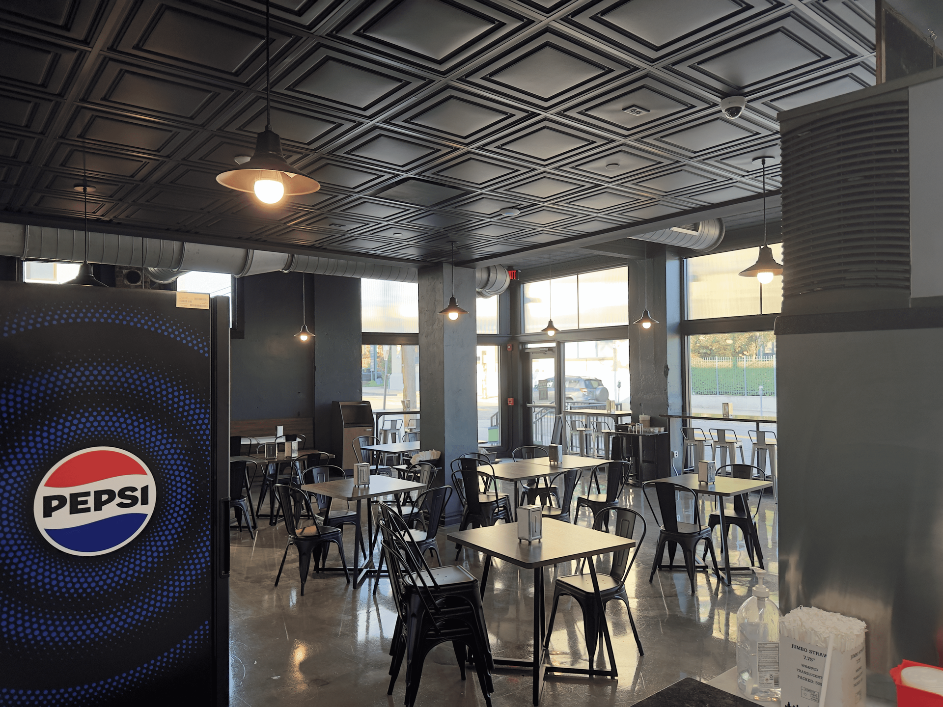 Empty Pepsi-branded cafe interior with tables, chairs, and large windows showing daylight outside