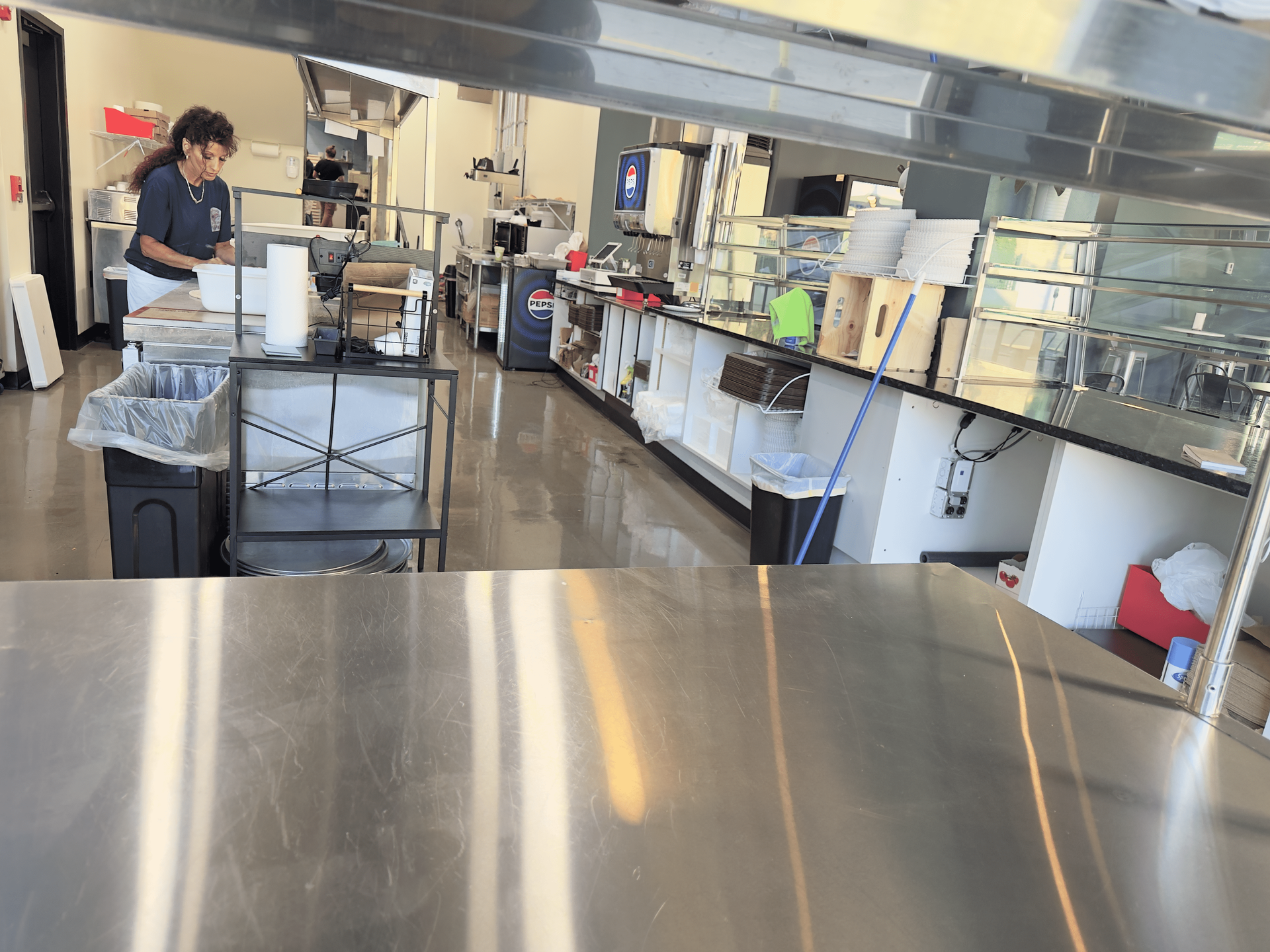 Commercial kitchen with a person preparing food near stainless steel counters and equipment.