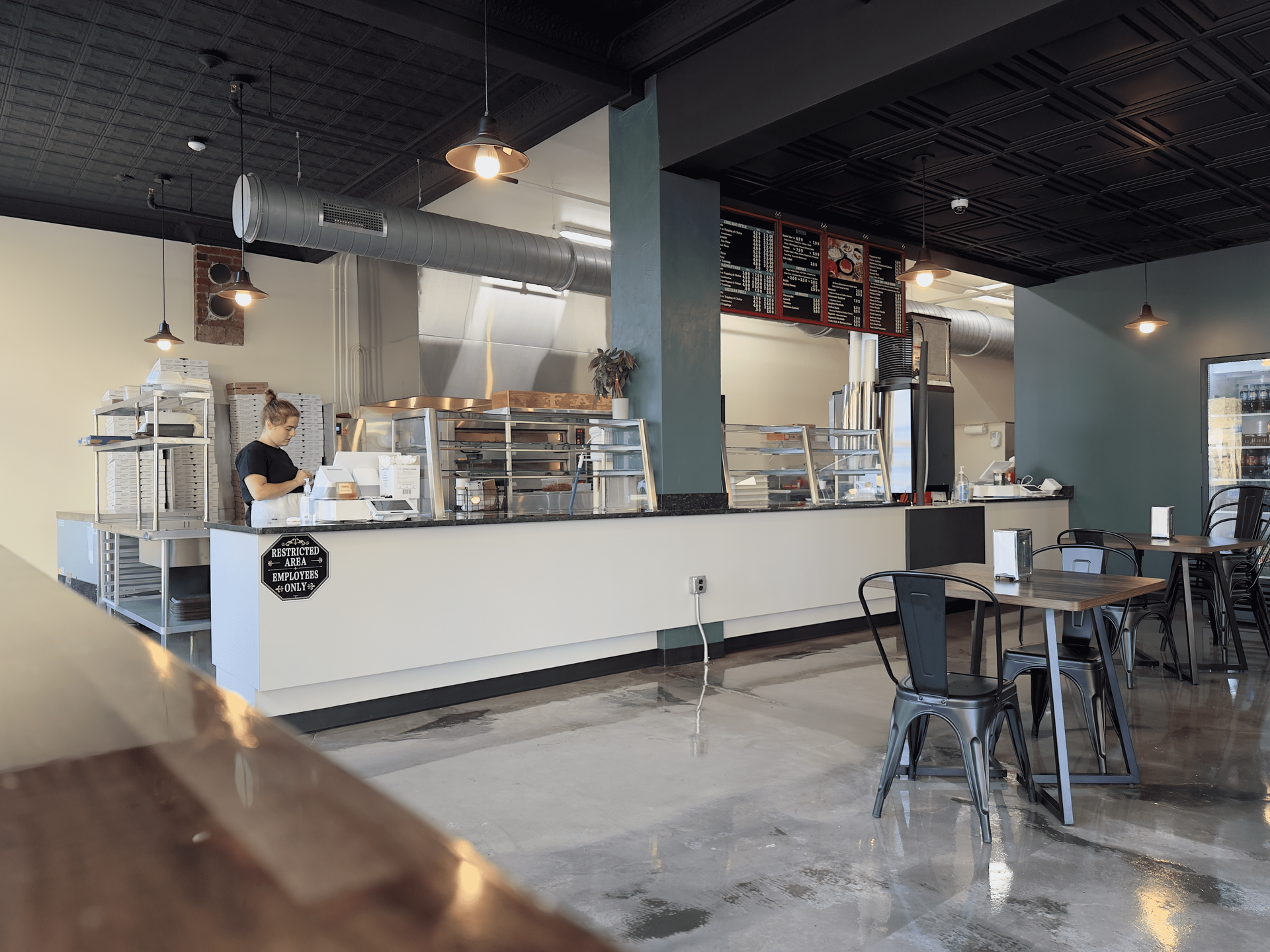 Modern café interior with a long counter, stools, tables, and an employee behind the bar