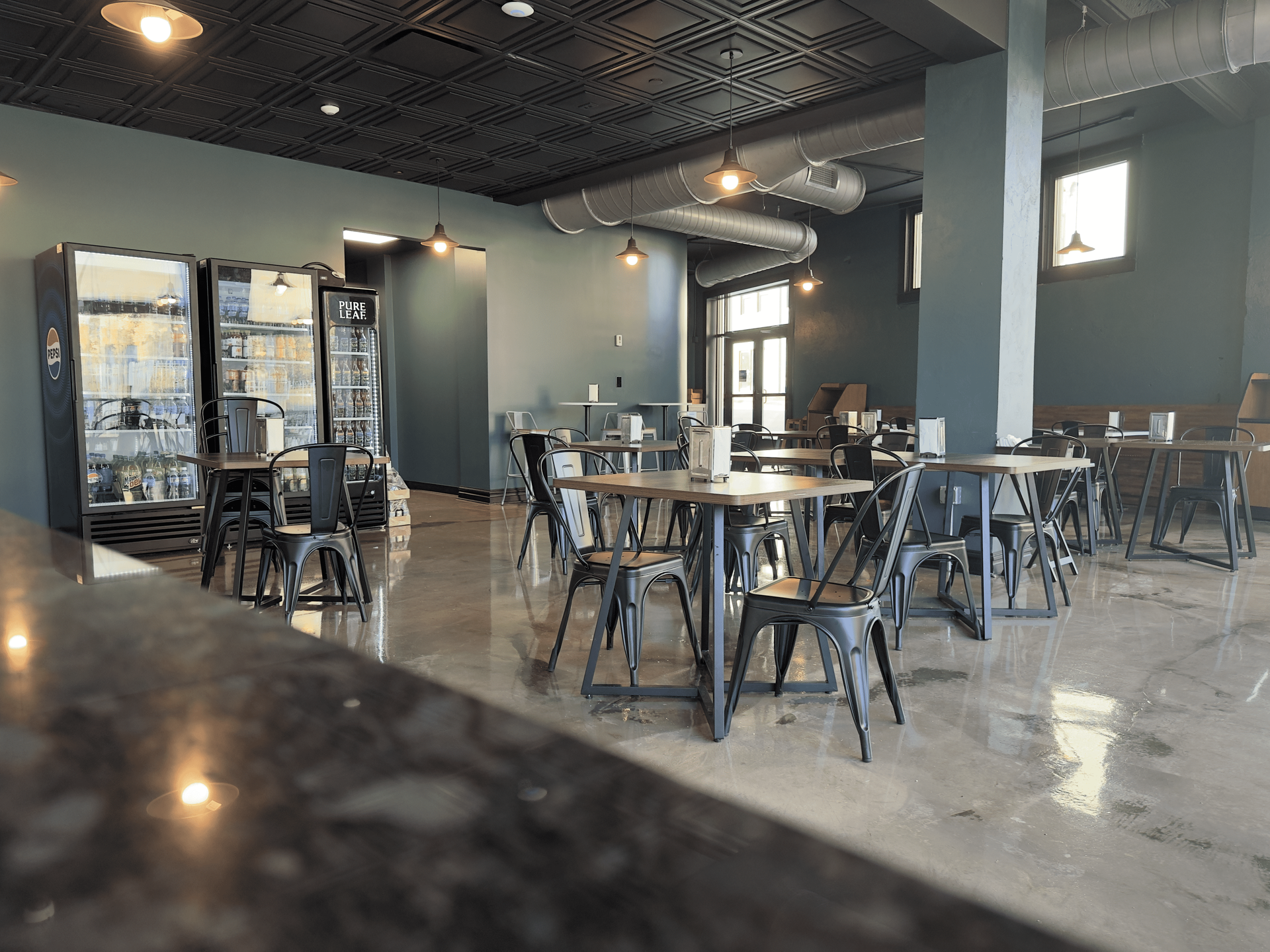 Empty modern café with metal tables and chairs, dark ceiling, and glossy concrete floor.