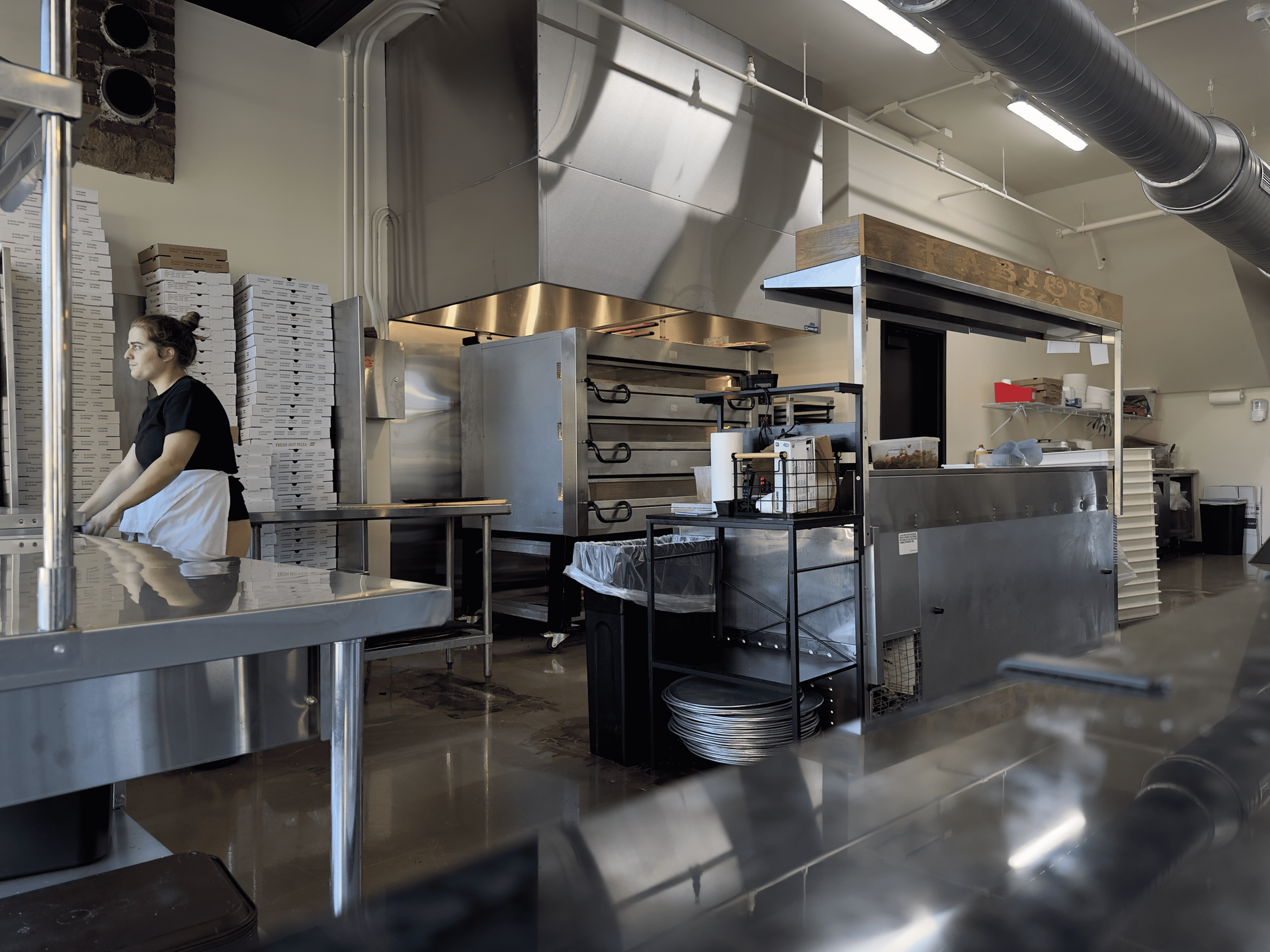 Commercial kitchen with stainless steel counters, ovens, and a worker standing near prep tables