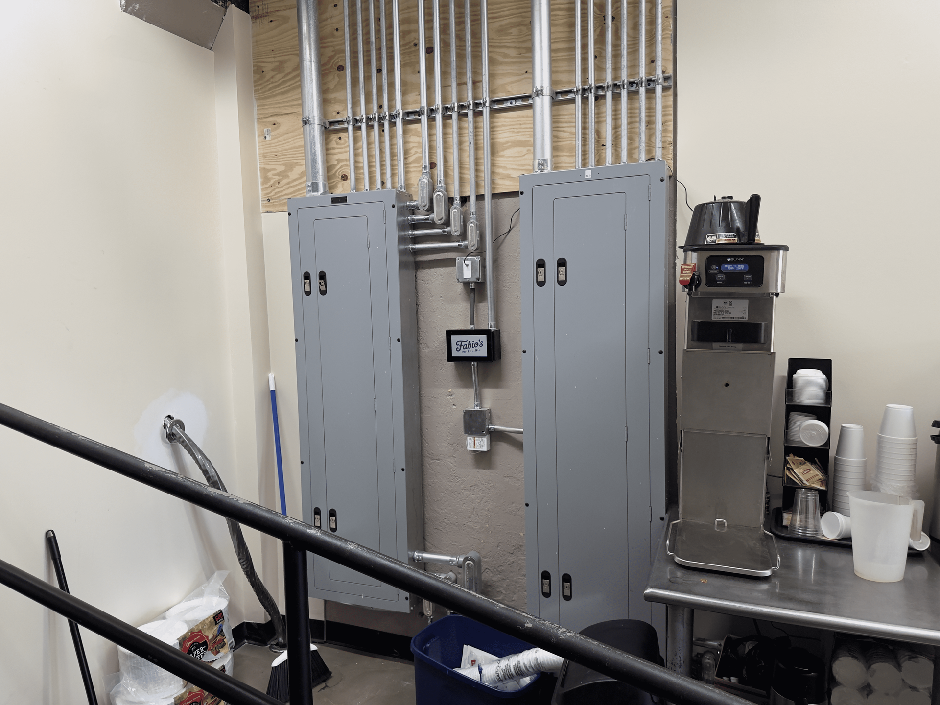 Industrial utility room with gray electrical cabinets, exposed pipes, and a stainless steel work table