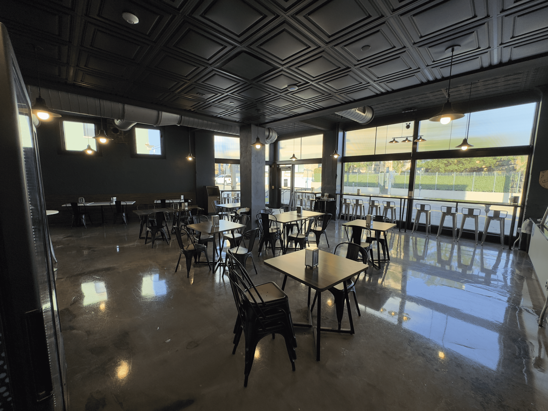 Empty café dining room with black tables and chairs, glossy floor, and large windows overlooking greenery