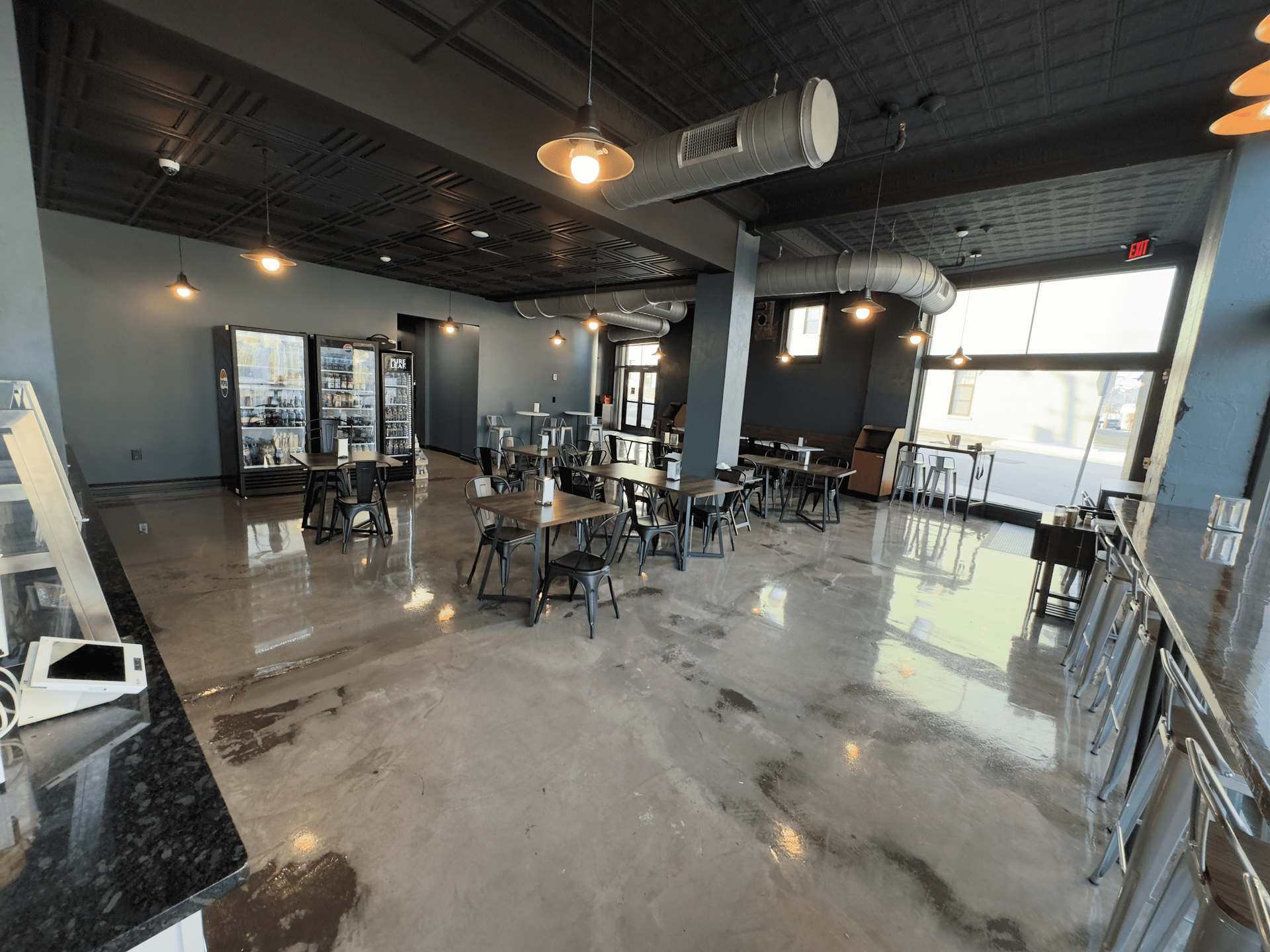 Modern cafe interior with polished concrete floors, black ceiling, and scattered tables and chairs.