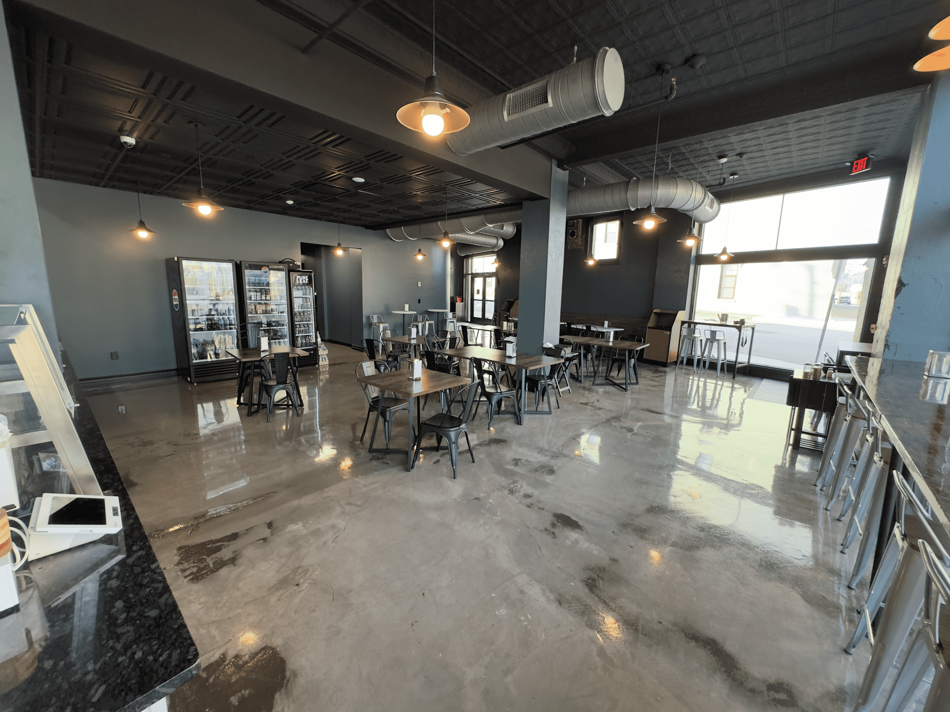 Modern open office lounge with tables, chairs, polished concrete floor, and large windows