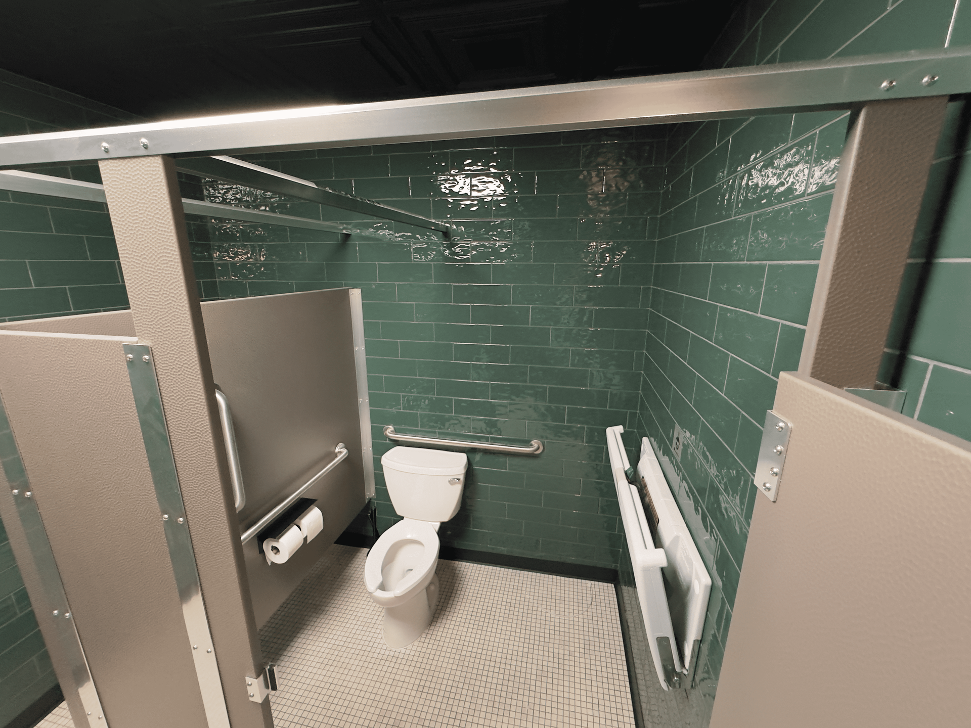 Public restroom stall with green tile walls, toilet, and grab bars, viewed through an open door