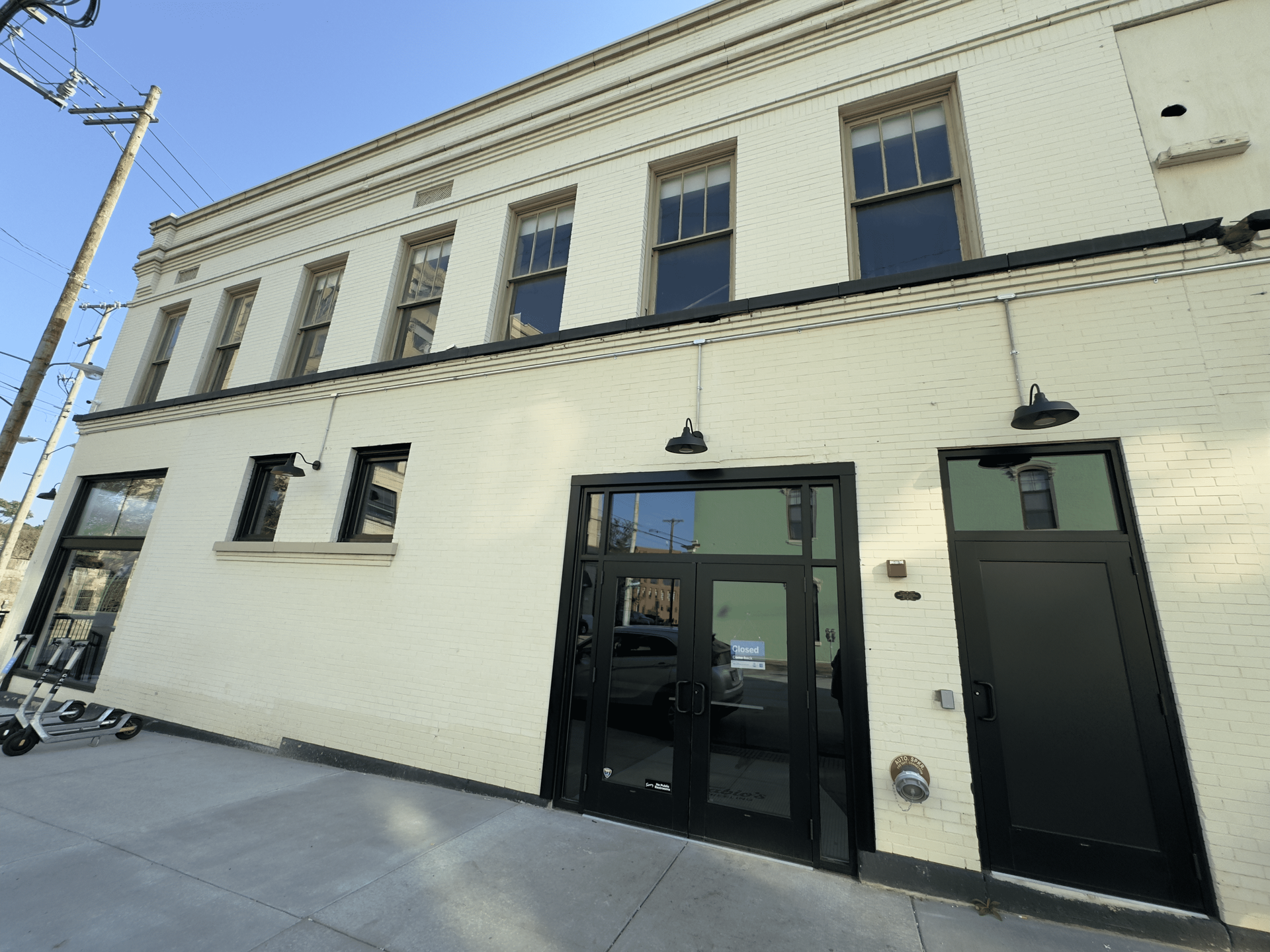 Street-level view of a cream-colored building facade with black doors and windows under a clear blue sky