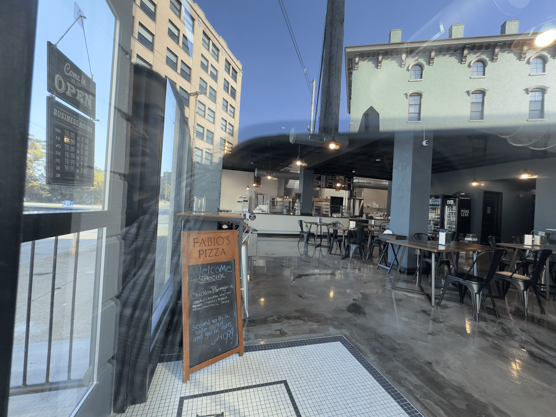 Outdoor café patio with tables and chairs beside a city street under a dark canopy.