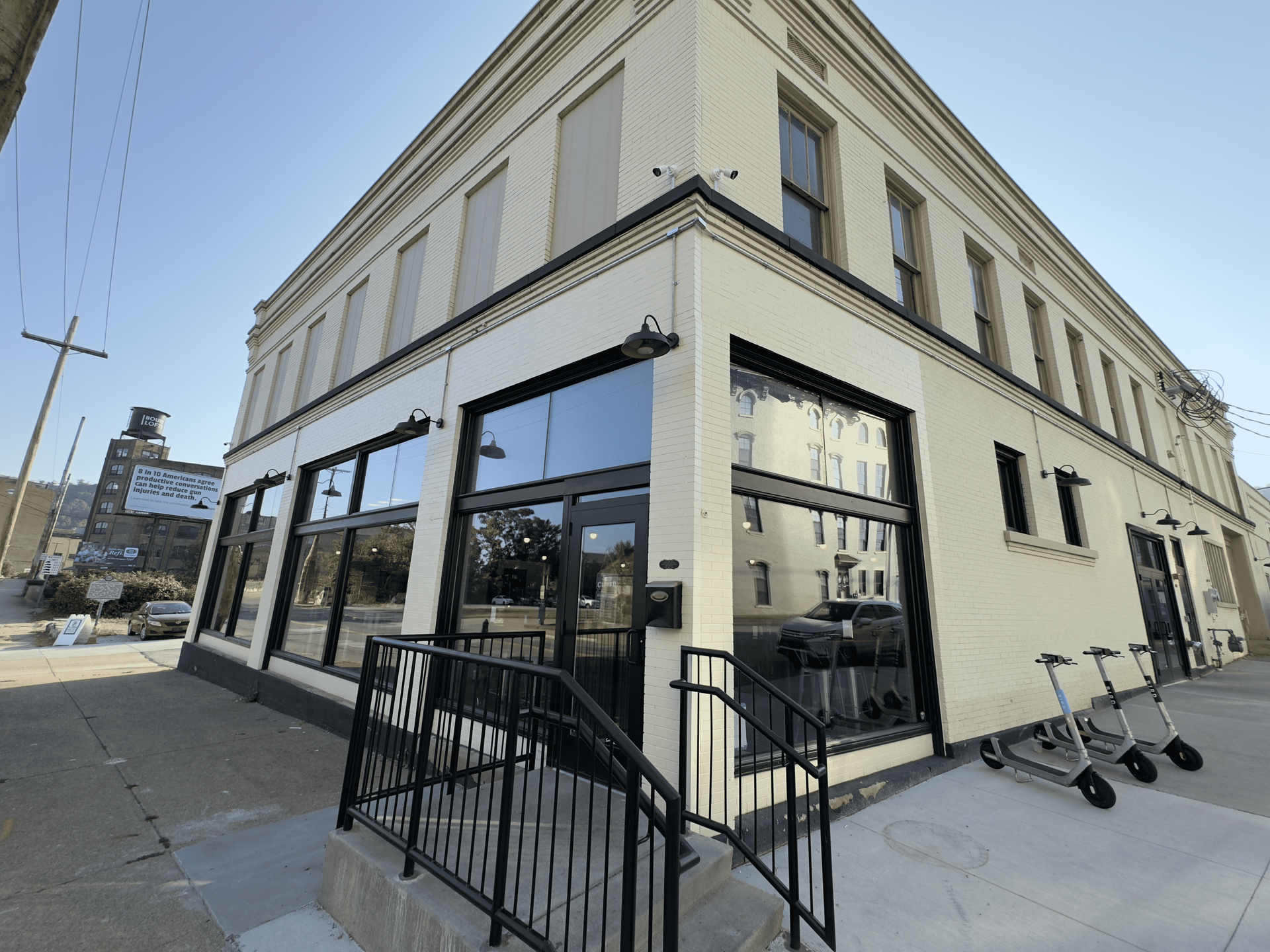 Corner café with large windows, black railing, and several parked scooters on a city sidewalk