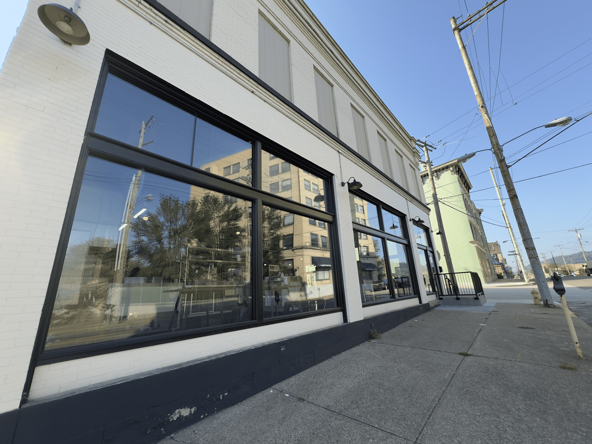 Empty storefront with large black-framed windows on a sunny city sidewalk.