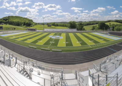 Empty football field with green turf, black track, and bleachers under a cloudy sky