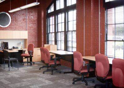 Empty office with red chairs, desks, and large windows along a brick wall