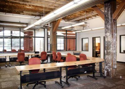 Open office conference room with long table, red chairs, exposed beams, and large windows