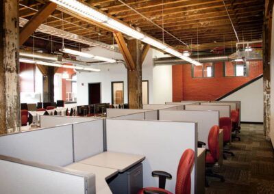 Open office with cubicles, red chairs, exposed wooden beams, and brick walls