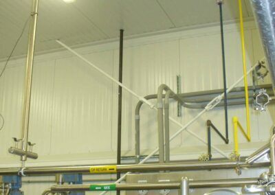 Industrial piping and hoses in a white utility room with yellow safety rails and metal scaffolding