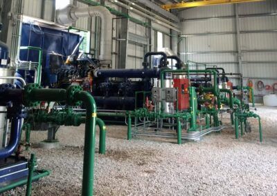 Industrial machinery and green piping inside a factory hall with gravel floor