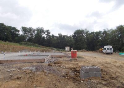 Construction site with concrete foundations, dirt lot, trees, and a white van in the background