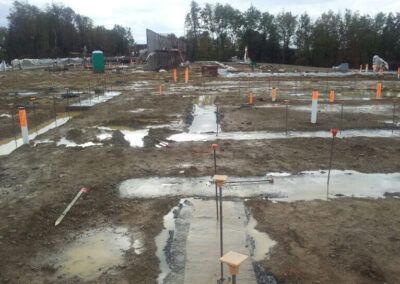 Muddy construction site with orange survey stakes and concrete footings laid out in a grid
