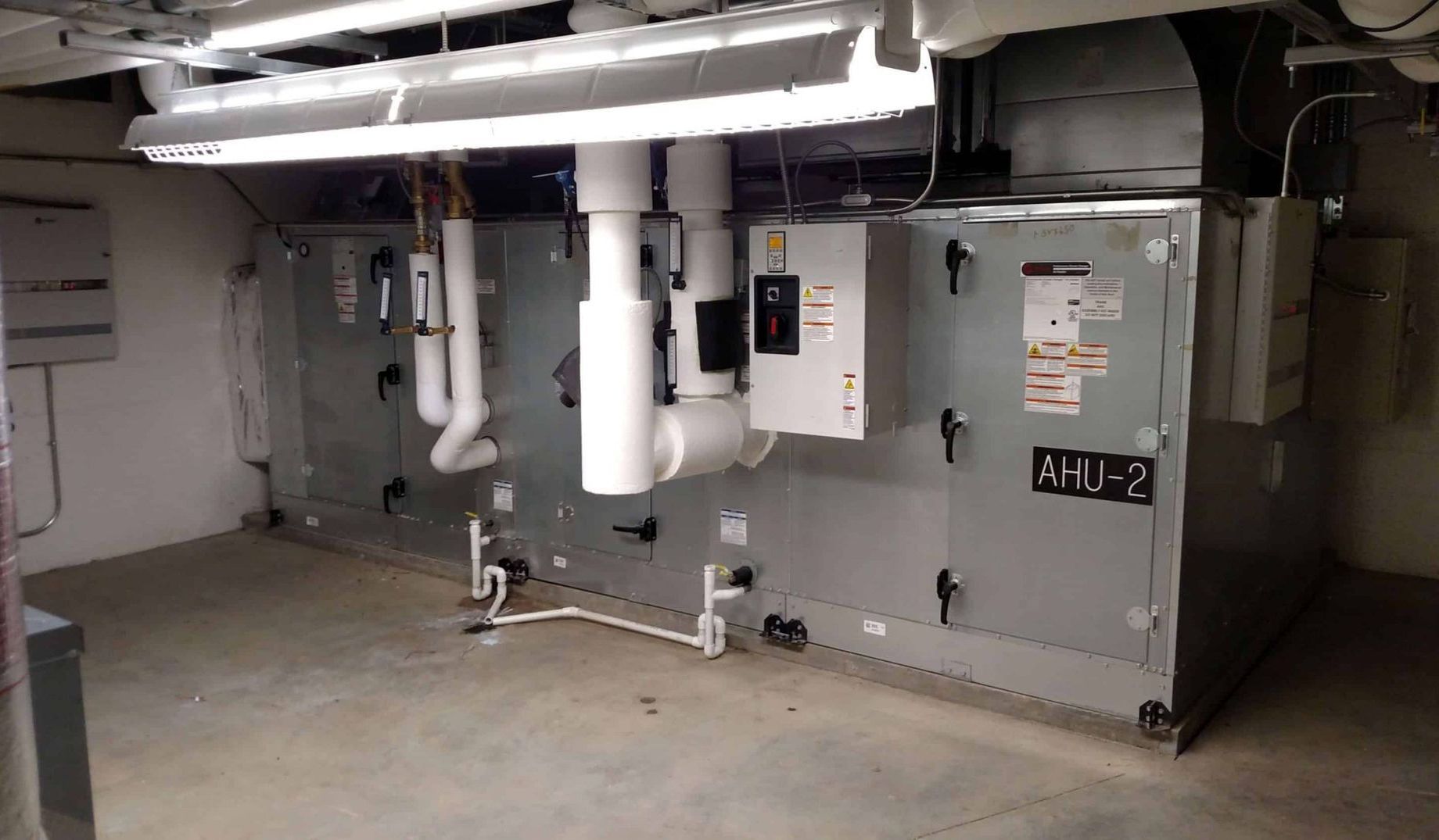 Basement mechanical room with large HVAC units, pipes, and ductwork.