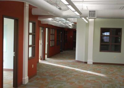 Empty indoor hallway with red doors, white walls, and patterned carpet flooring