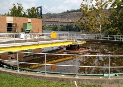 Circular water treatment tank with yellow bridge railing and surrounding fence in an industrial setting