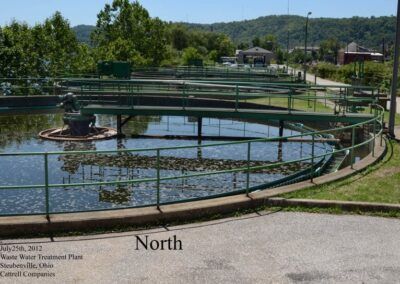 Circular water treatment basin with green railings in a park, with hills in the background