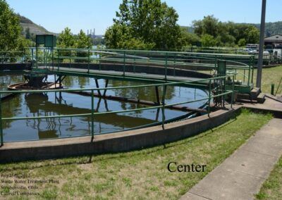 Circular water treatment tank with metal walkway and railing in a grassy outdoor facility