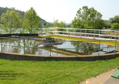 Circular water treatment tanks in a grassy park with trees and hills in the background