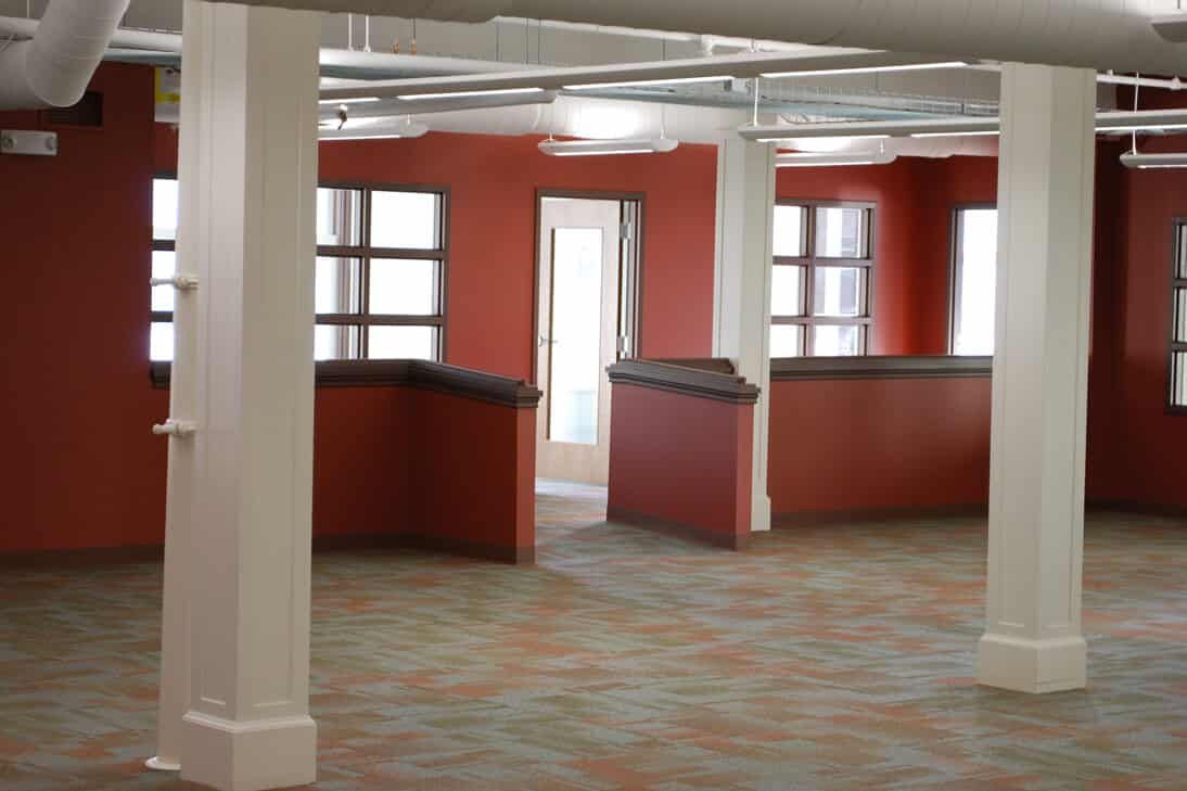 Empty office space with red walls, white columns, and carpeted floor