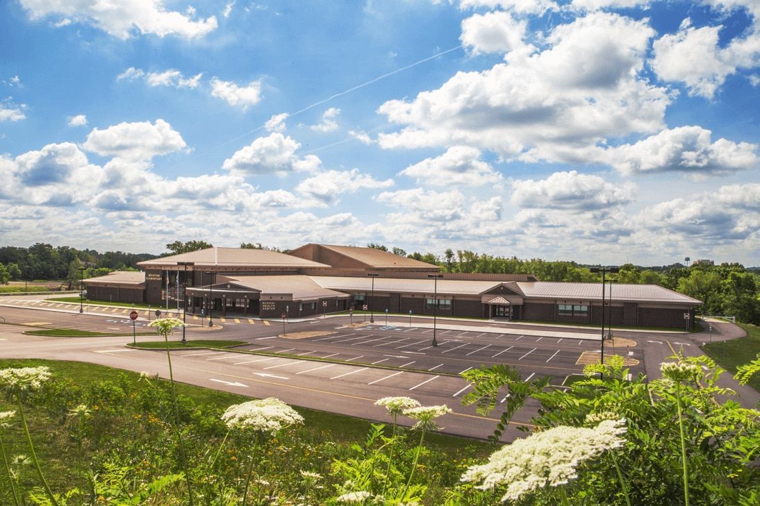 Wide view of a large beige building and empty parking lot under a bright, cloudy sky