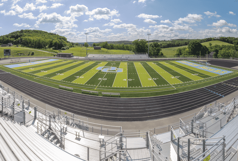 Empty stadium with green-striped field and running track under a cloudy sky