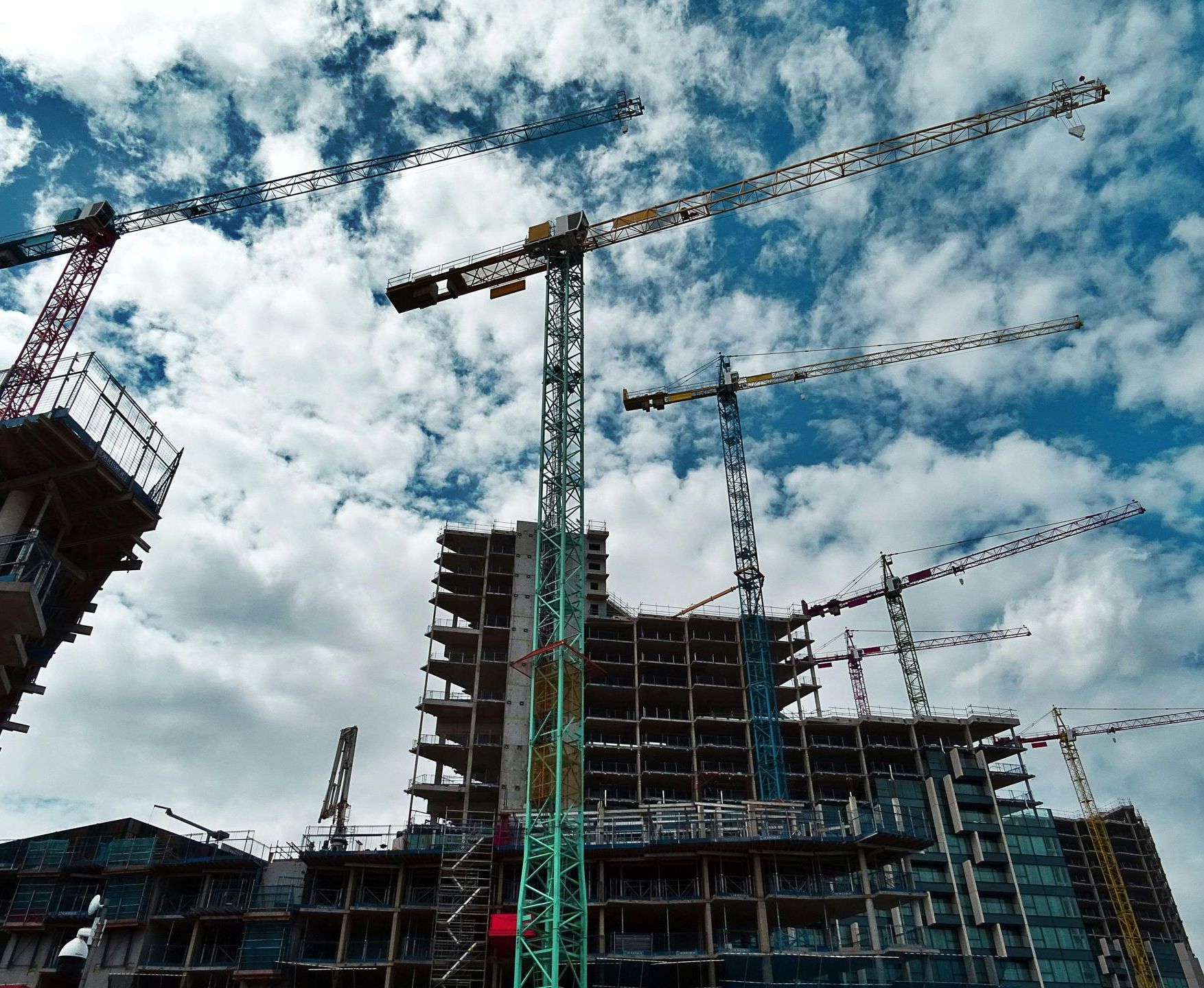 Construction site with tall cranes and multi-story building framework under a cloudy blue sky