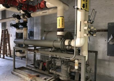 Industrial machinery and pipes in a utility room, with red and white piping and valves.