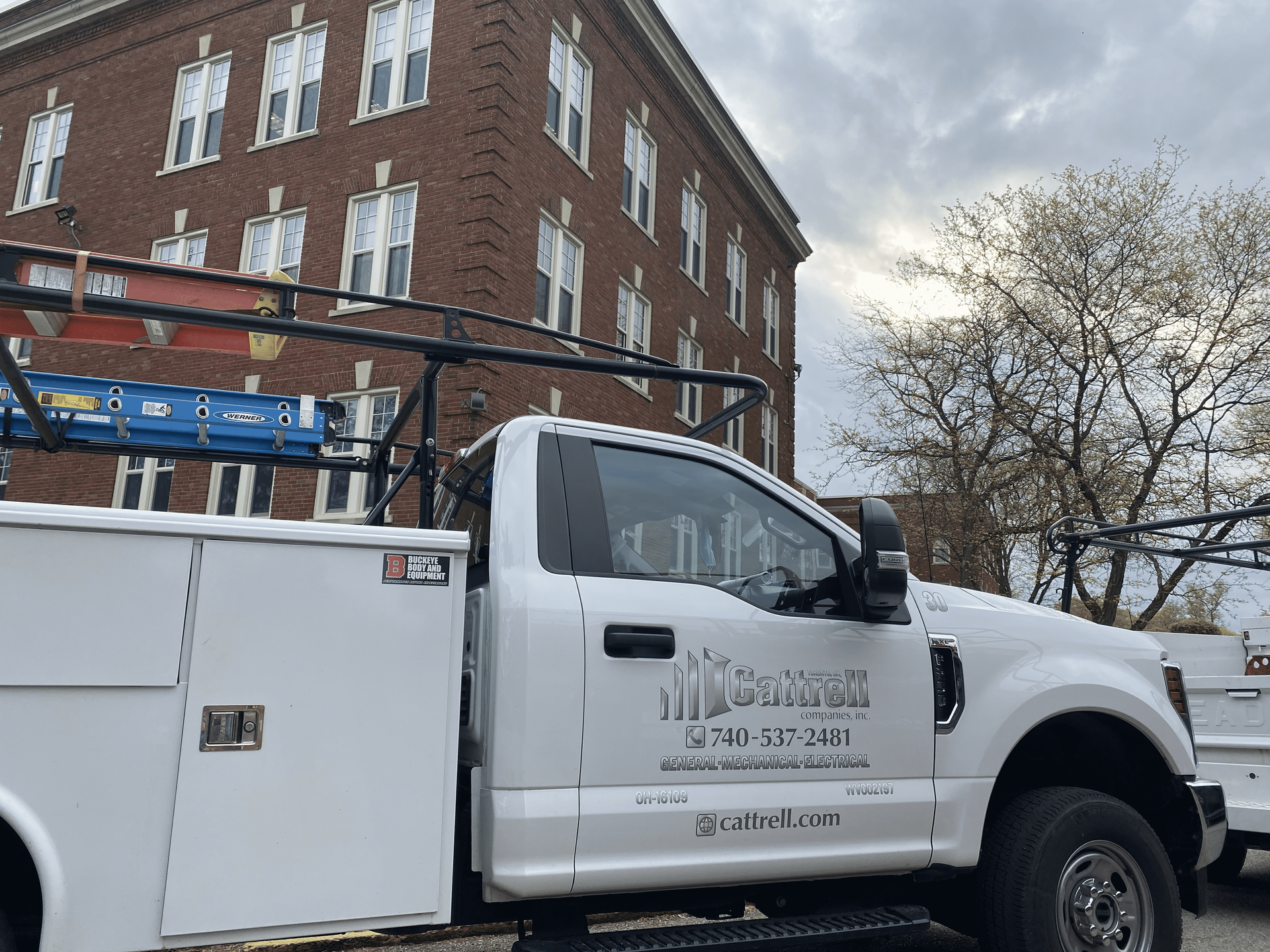 White utility truck parked by a red brick building on a city street