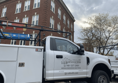 White utility truck parked beside a brick building on a cloudy day