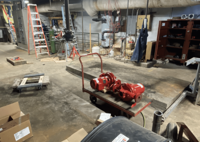 Basement utility room with pipes, ladder, shelving, and a red pump on a wheeled cart on concrete floor