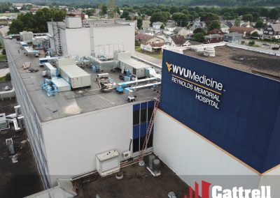 Aerial view of a large white hospital building with a blue wall sign and rooftop equipment in a suburban area