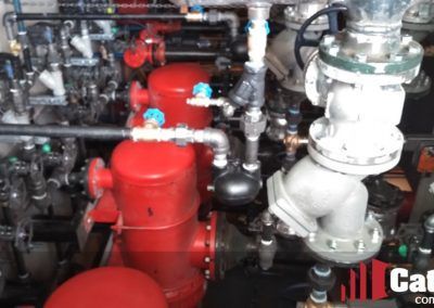Red industrial piping and valves in a machinery room, with a large white pump assembly on the right.