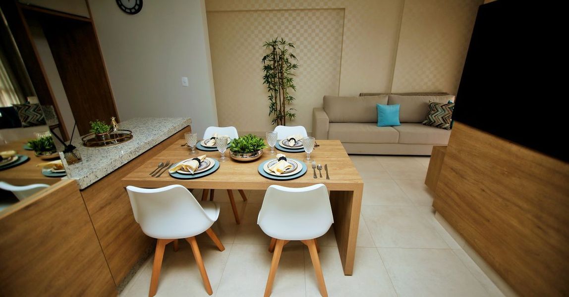 Comedor moderno con mesa puesta, sillas blancas y sofá beige al fondo.