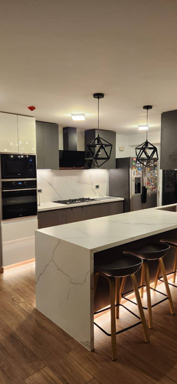 Cocina moderna con isla blanca, armarios oscuros, suelos de madera y lámparas colgantes.