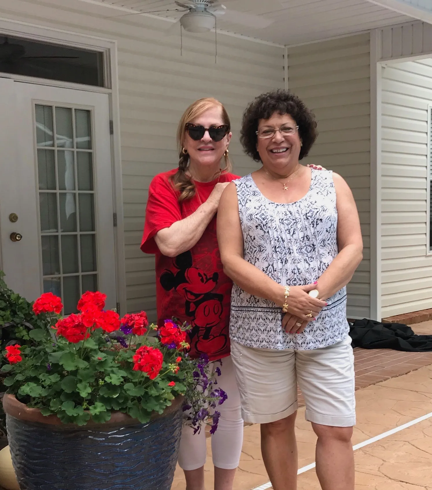 Two women standing next to a potted plant with red flowers
