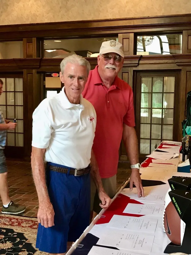 Two men are standing next to each other in front of a table.